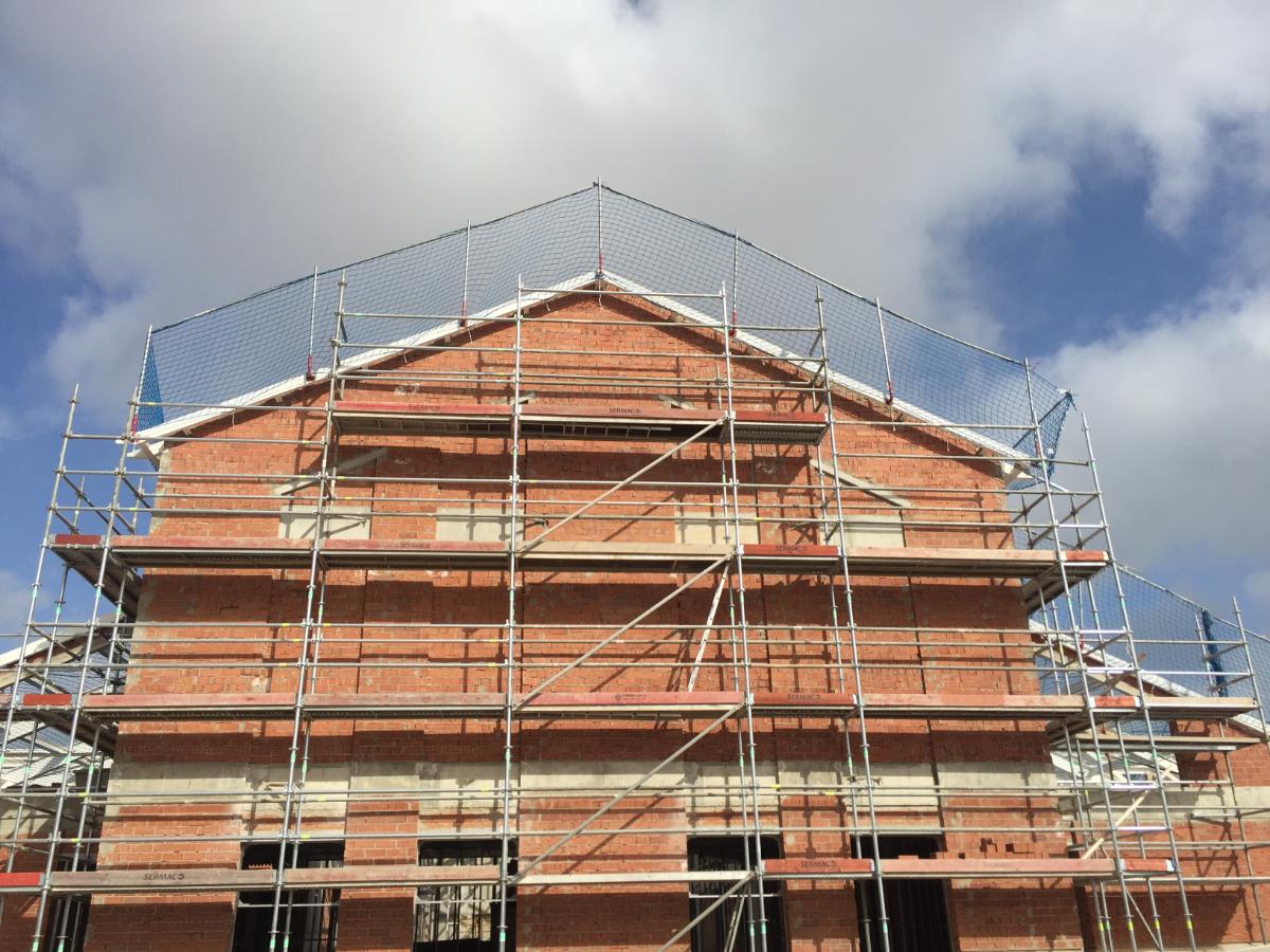 Andamio metálico montado sobre la fachada de ladrillo de un edificio en construcción, cubierto en la parte superior con una red de seguridad (protección colectiva) para trabajos verticales en Guipúzcoa.